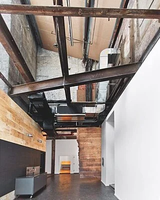 Loft com pé-direito duplo e vigas metálicas aparentes pintadas de preto.